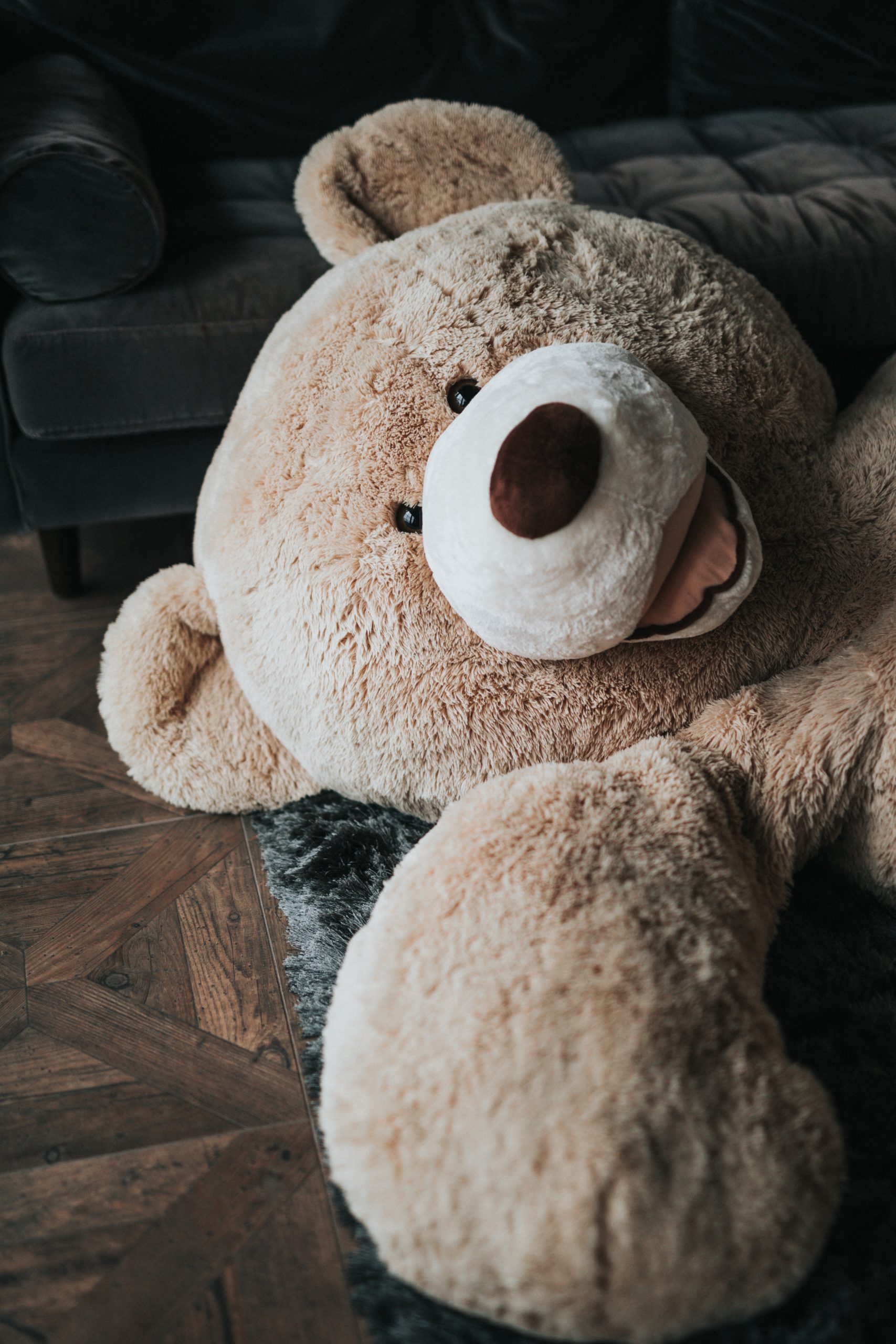 Giant teddy bear lounging on a rug.