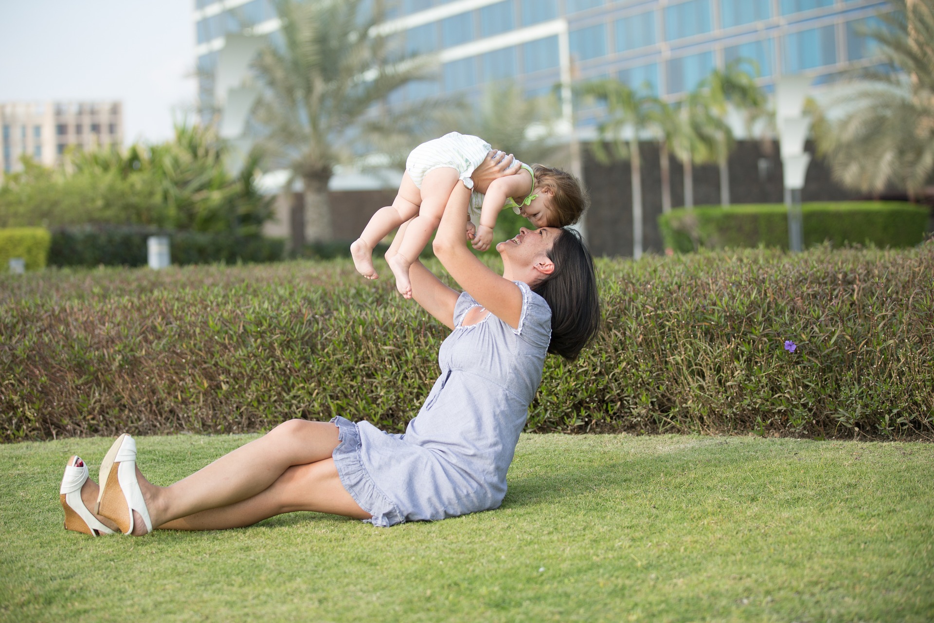 A woman holding a baby up in the air while sitting on the grass.