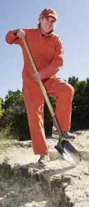 Louis Sachar in an orange jumpsuit and hat. He is posing with a shovel pretending to dig.