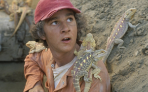 Stanley in a hole covered in yellow-spotted lizards. He is looking up towards the right, possibly talking to someone.