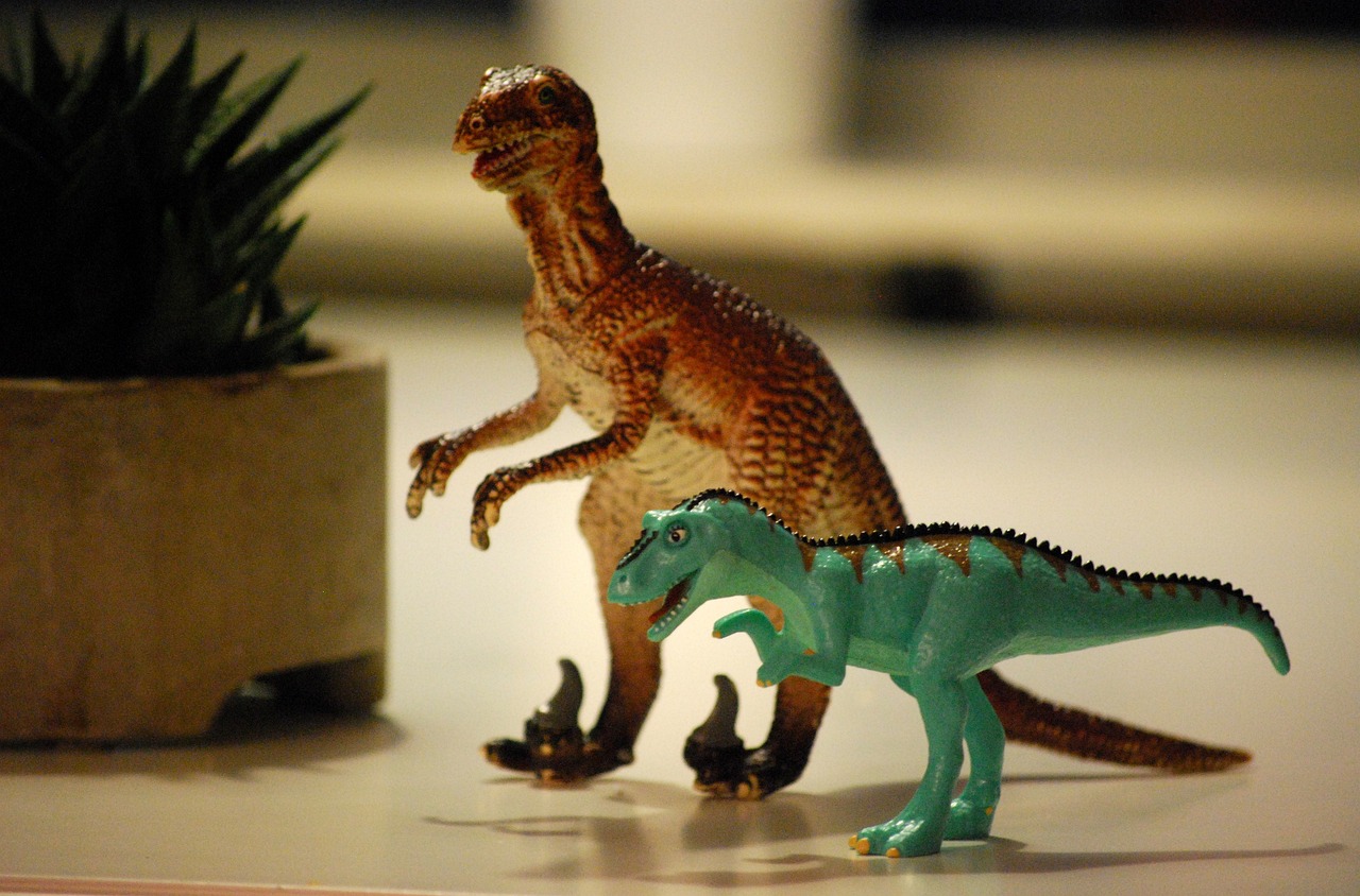 Two plastic dinosaur toys sitting by a potted plant.