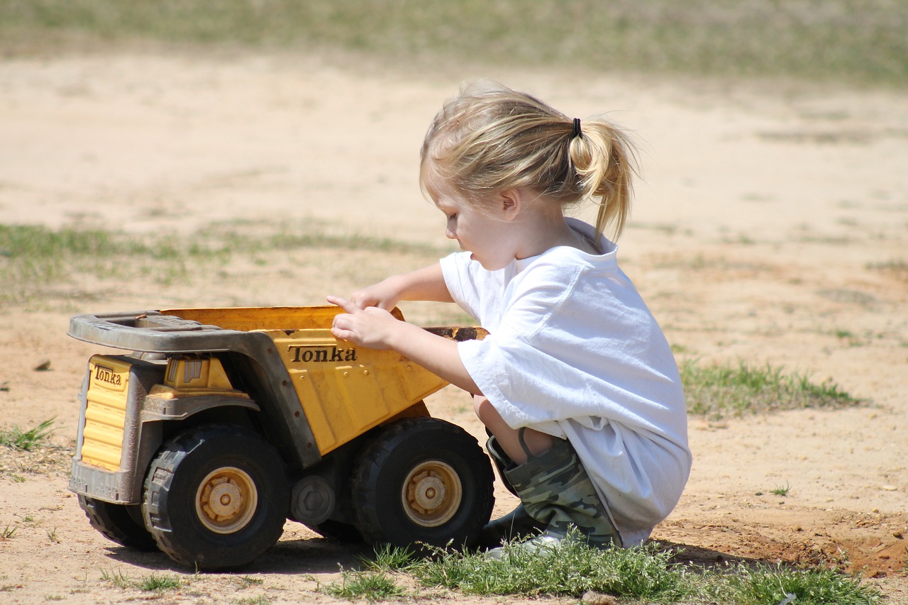 Little girl playing with a toy dump truck in the dirt
