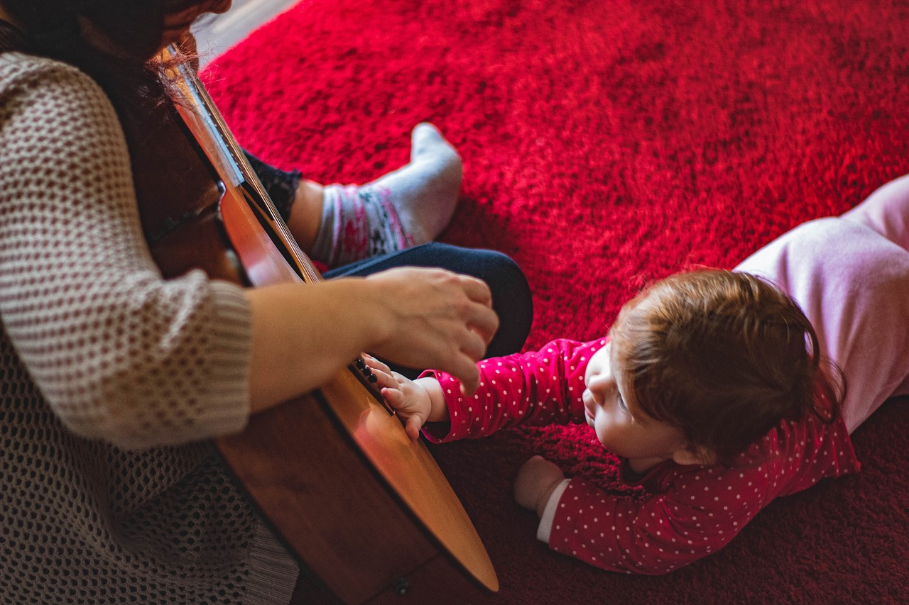 A toddler touches a guitar while a grown up is playing.