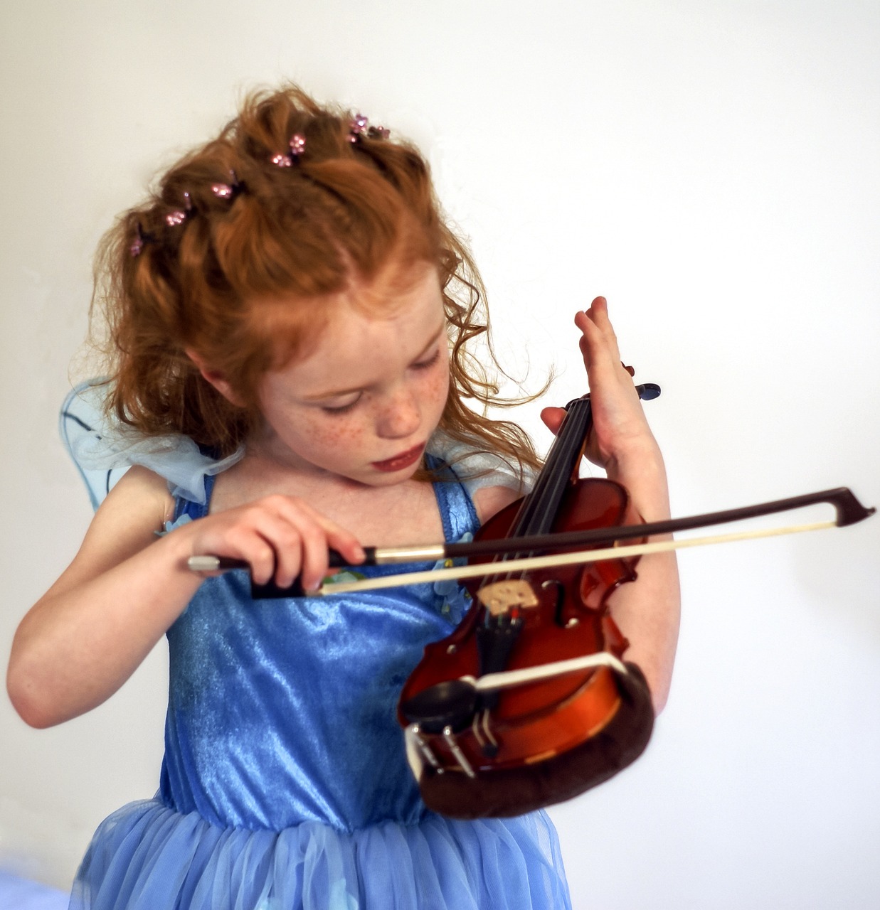 Girl in a blue fairy dress playing the violin with her bow.