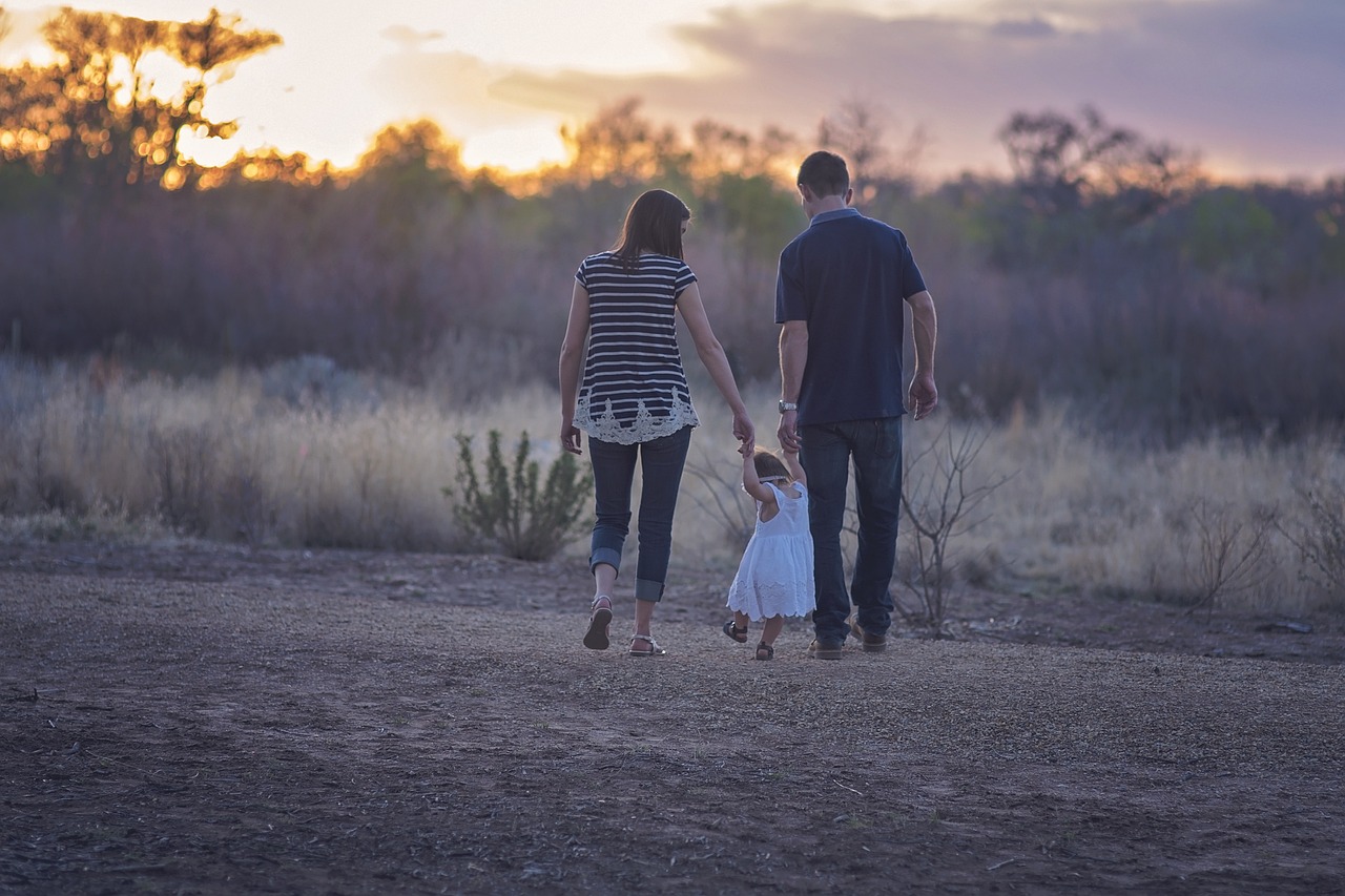 Two adults walking with a child, holding hands as they go down the dirt road.
