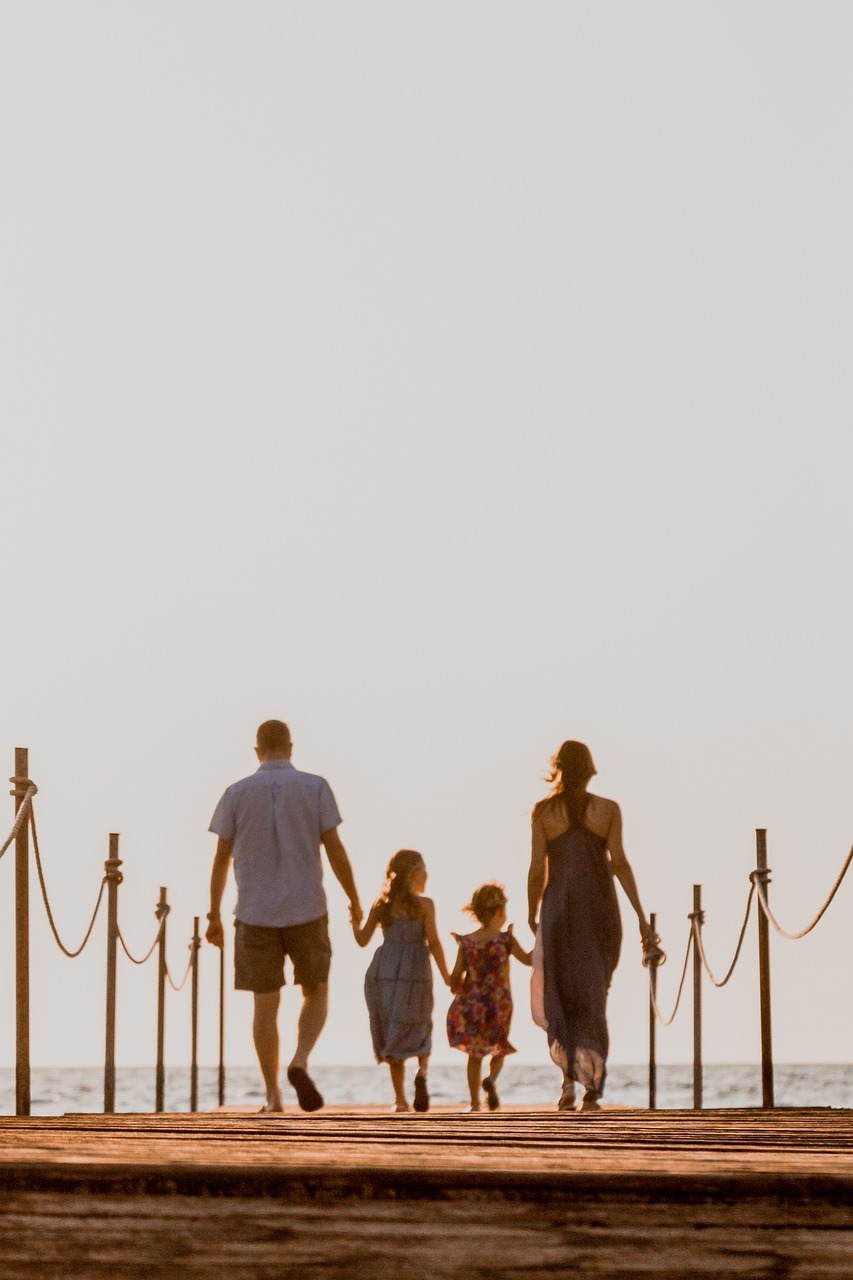 A family walking on a boardwalk toward the water.