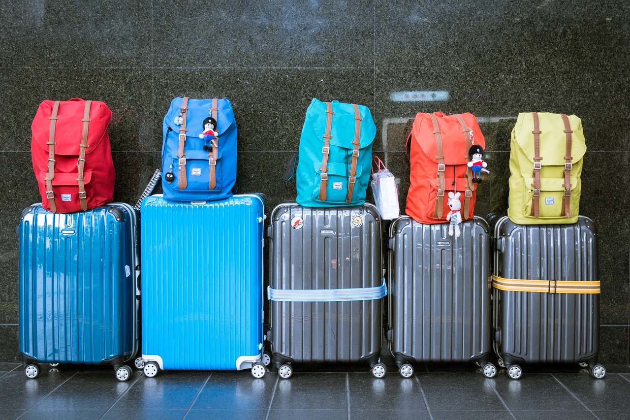 Colorful backpacks sitting on top of rolling suitcases ready for their next travel adventure.