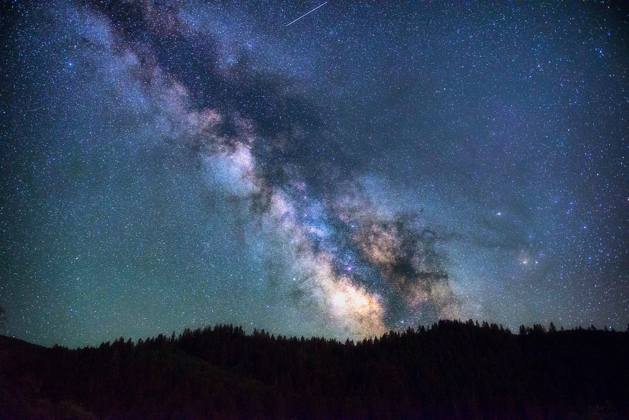 The night sky with stars and the milkyway above mountains and trees.