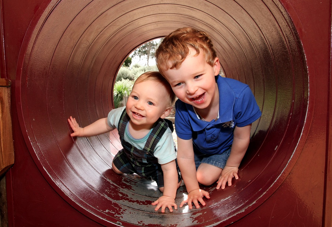 Two happy children playing in a tunnel on a playground.