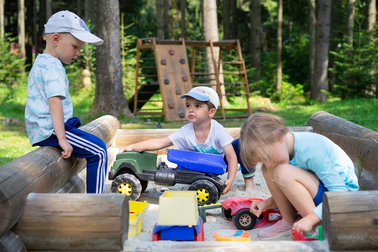 Children playing in a sandbox with trucks and toys.