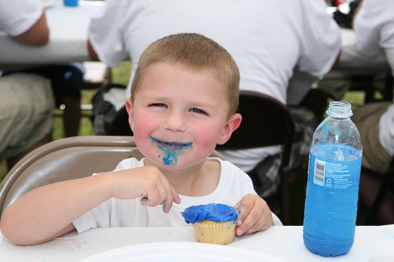 A boy enjoying a blue frosted cupcake and very blue water.