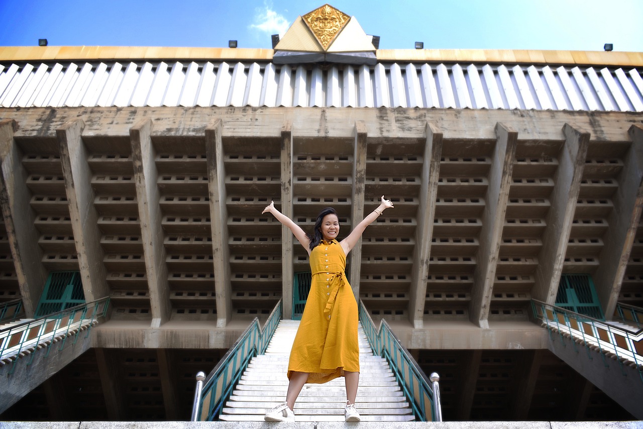 Woman in yellow looking confident and happy in front of stairs.