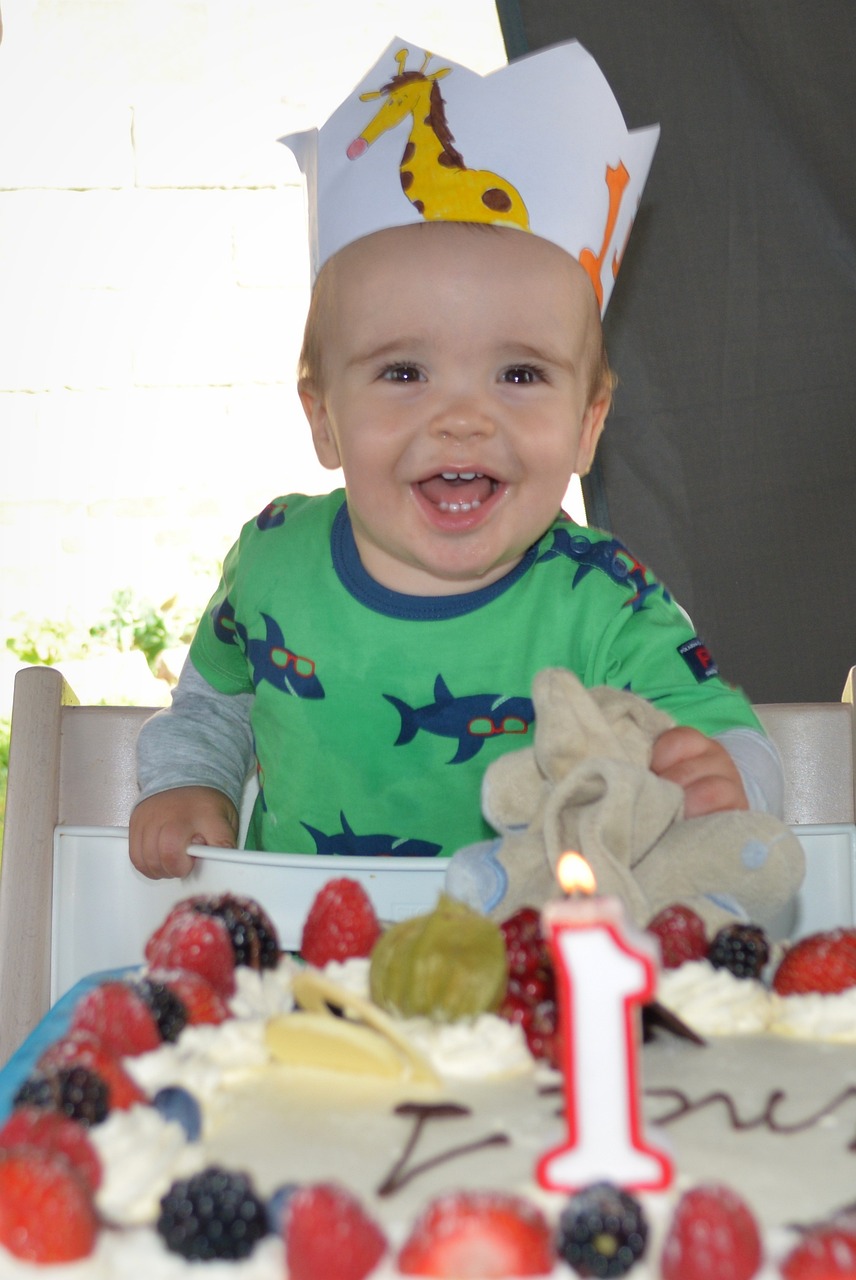 A small child wearing a birthday crown with a number 1 candle in their cake.