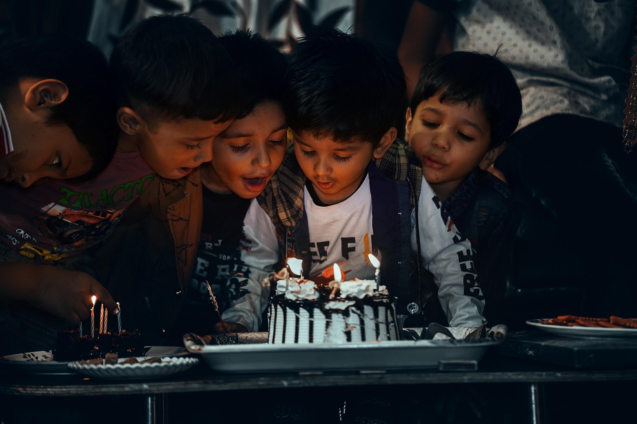 A crowd of boys surrounding a cake with the glow of candles on their faces, preparing to blow.