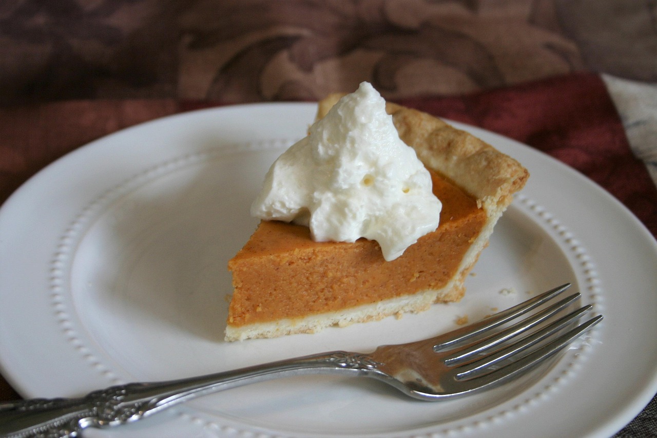 A slice of pumpkin pie with a dollop of whipped cream ready to eat.