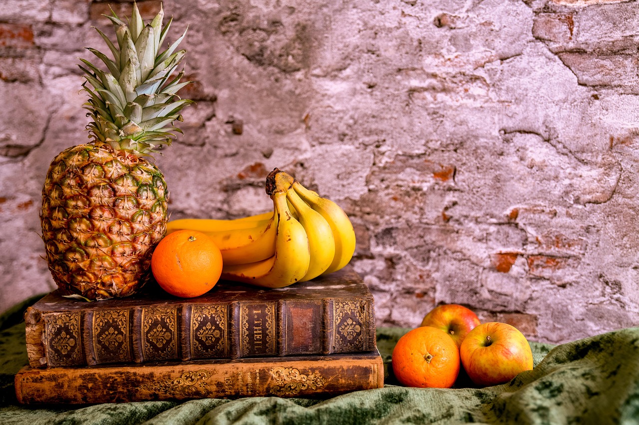 Pineapple, orange, and bananas resting on top of a couple of books.